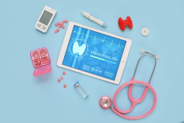 Tiroit bezi modelli tablet bilgisayar, glukometre ve steteskop mavi arka planda. Endokrinoloji kavramı