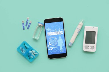 Yeşil arka planda cep telefonu, tükenmez kalem, glukometre ve insülin. Endokrinoloji kavramı