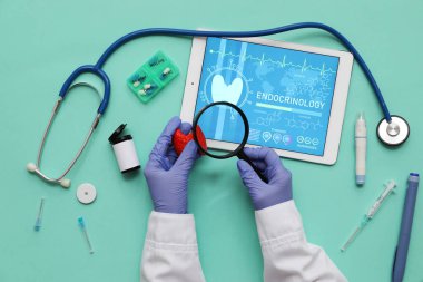 Doktor yeşil arka planda tiroit bezi modeli, büyüteç ve tıbbi malzeme tutuyor. Endokrinoloji kavramı