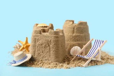 Deniz kabukları ve mavi arka planda mini şezlongla güzel bir kumdan kale.