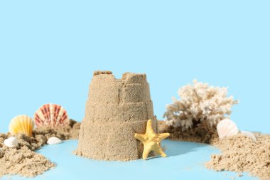 Mavi arka planda deniz yıldızı ve deniz kabukları olan güzel bir kumdan kale.