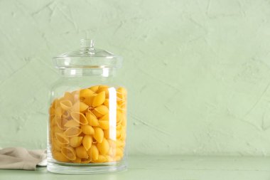 Yeşil arka planda çiğ koni makarnalı kavanoz.