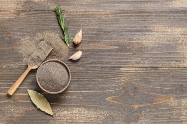 Ahşap zemin üzerinde defne yaprağı, sarımsak ve biberiye olan bir kase karabiber tozu.