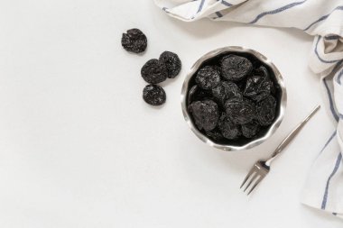 Beyaz zemin üzerinde kuru erik olan metal kase.