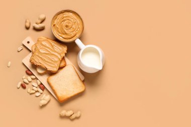 Fıstık ezmeli kase, bir sürahi süt, bej arka planda tost ve fındık.