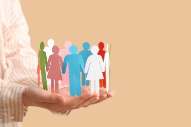 Renkli arka plana karşı kağıt insan figürleri olan kadın eller, yakın plan. Çeşitlilik ve kapsama kavramı