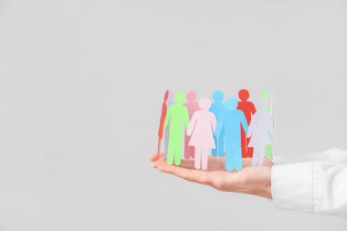 Gri arkaplan üzerinde kağıt insan figürleri olan kadın eller, yakın plan. Çeşitlilik ve kapsama kavramı