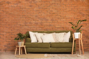 Dekoratif yastıklı yeşil kanepe ve odada tuğla duvarın yanında bitkiler.