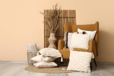 Dekoratif yastıklı koltuklar ve bej duvarın yanında otlar.