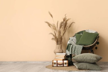 Kol sandalyesi yeşil ekose, dekoratif yastıklar ve bej duvarın yanında otlar.