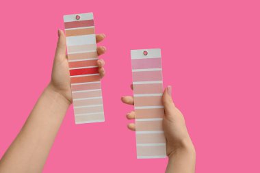 Pembe arka planda boya rengi paletleri olan kadın elleri, yakın plan.