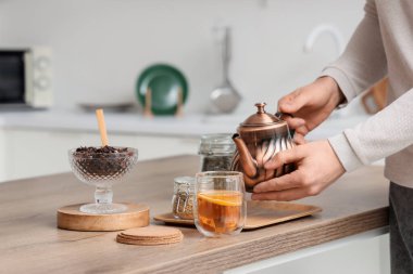 Çaydanlık ve cam bardak limonlu genç adam mutfaktaki masada, yakın plan.