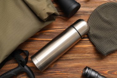 Modern termos, sırt çantası, şapka ve ahşap arka planda seyahat için eşyalar