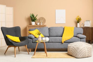 Oturma odasının içinde kanepe, koltuk ve vazoda mimoza çiçekleri var.