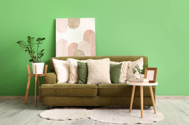 Yastıklı rahat kanepe, çiçek ve yeşil duvarın yanındaki sehpa.