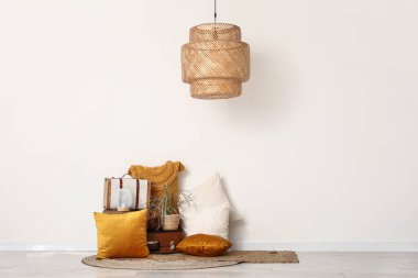 Beyaz duvarın yanında yastıklar, çiçek ve bavul var.