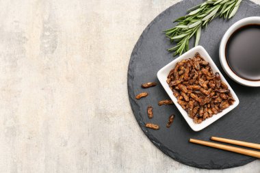 Gri arka planda biberiye ve soya soslu bir kase kızarmış böcek.