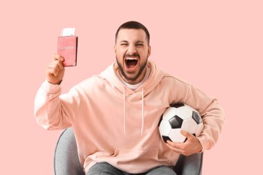 Pasaport ve biletlerle çığlık atan futbol fanatiği pembe arka planda koltukta oturuyor.