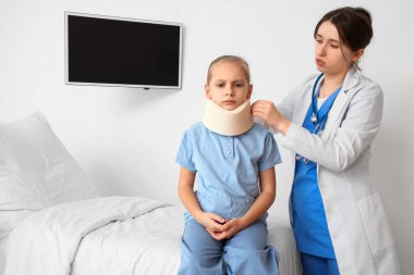 Doktor klinikte küçük kızın boynuna boyun tasması takıyor.