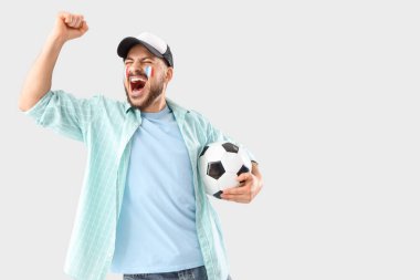 Yüzünde Fransa bayrağı ve arka planında futbol topuyla bağıran erkek taraftar.