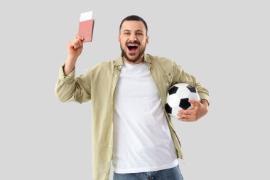 Pasaportu, biletleri ve arka planda futbol topu olan mutlu bir erkek taraftar.