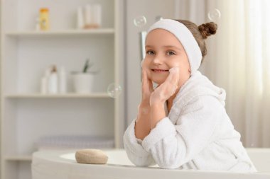 Banyoda sabun ve köpüklü küçük bir kız.