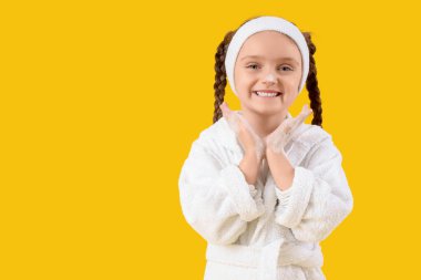 Sarı arka planda köpüklü bornoz giyen küçük kız.