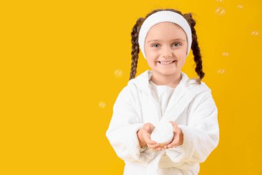 Bornozlu, sabunlu ve sarı arka planda köpüklü küçük kız.