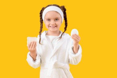 Sarı arka planda sabunlukları olan bornozlu küçük bir kız.