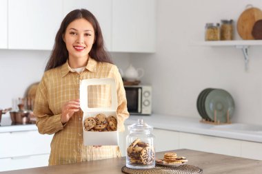 Mutfakta bir kutu kurabiyeyle genç bir Asyalı kadın.