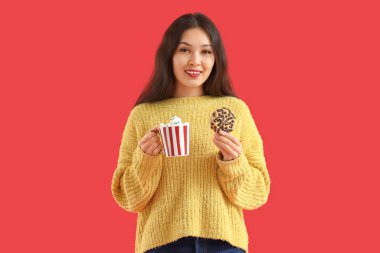 Kırmızı arka planda kurabiye ve bir fincan kakaolu genç Asyalı kadın.