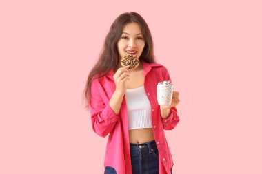 Kurabiye ve pembe arka planda bir fincan kakaolu genç Asyalı kadın.