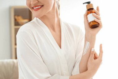 Genç bir kadın evde koluna krem sürüyor, yakın plan.