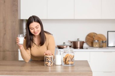 Mutfaktaki masada süt ve kurabiyeli genç kadın.