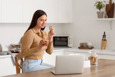Mutfaktaki masada elinde kahve ve kurabiye olan genç bir kadın.