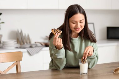 Genç bir kadın mutfakta süte kurabiye bandırıyor.