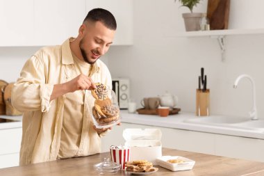 Genç adam mutfakta kavanozdan kurabiye alıyor.