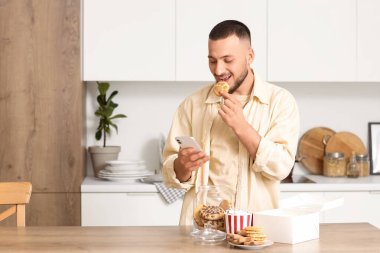 Cep telefonlu genç adam mutfakta pençe şeklinde kurabiye yiyor.