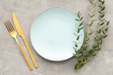 Gri grunge arka planında tabak, çatal bıçak ve bitki dallarıyla şık masa ayarları