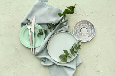 Yeşil grunge arka planında tabak, çatal bıçak ve okaliptüs dallarıyla şık masa ayarları