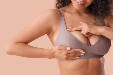 Genç Afro-Amerikalı kadın göğsünü bej arka planda kontrol ediyor, yakın plan. Kanser farkındalığı kavramı