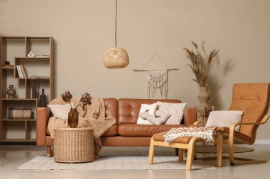 Rahat bir kanepe, ayak sehpası ve vazo içinde kurutulmuş çiçekler oturma odasının iç kısmında sepette.