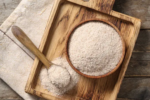 Tahta arka planda psyllium kabuğu tozu olan kase ve kaşık.