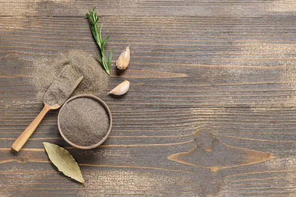 Ahşap zemin üzerinde defne yaprağı, sarımsak ve biberiye olan bir kase karabiber tozu.