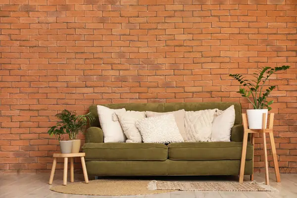 Dekoratif yastıklı yeşil kanepe ve odada tuğla duvarın yanında bitkiler.