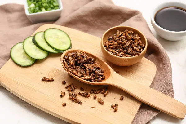 Kızarmış böcekli ahşap kase, beyaz arka planda salatalık ve soya sosu dilimleri.