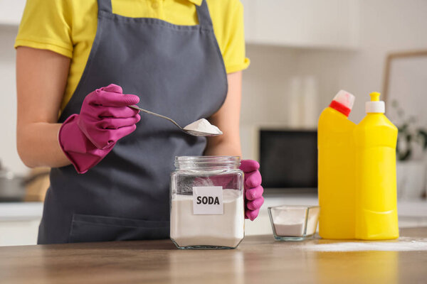 Young woman taking spoon of baking soda from jar for cleaning in kitchen, closeup