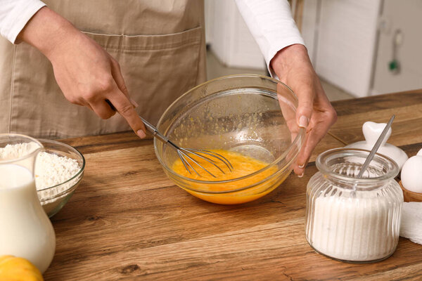 Женщина взбивает яйца с сахаром на столе на кухне. Крупный план