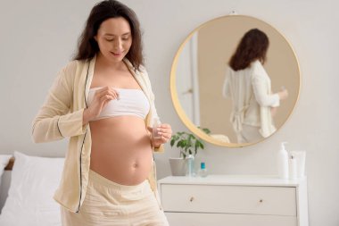 Yatak odasında kozmetik serumu olan hamile bir kadın var.