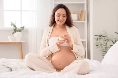 Yatak odasında vücut kremi olan hamile bir kadın.